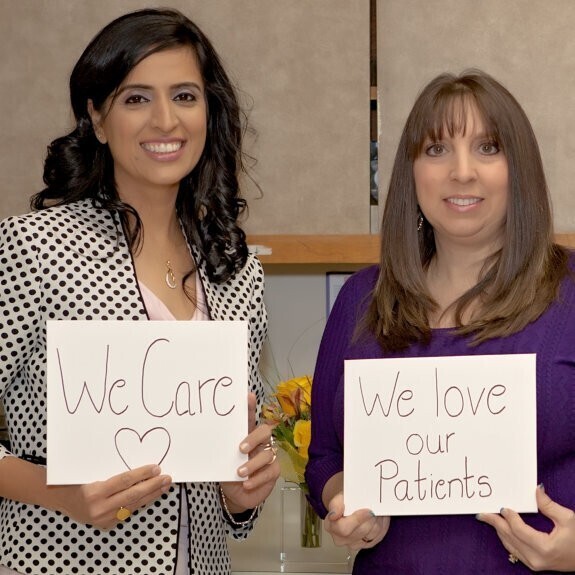 Two dental team members holding signs that say We Care and We love our Patients.