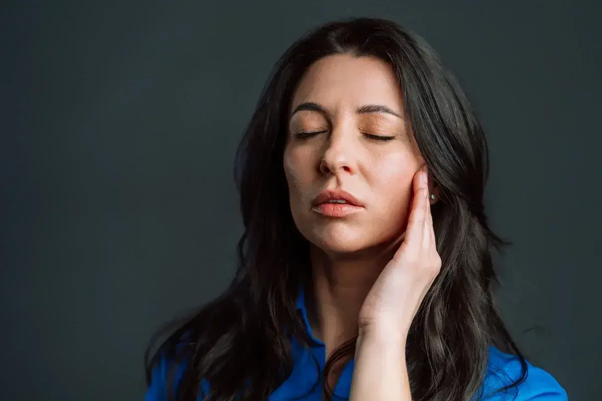 Woman experiencing jaw pain, holding her cheek with eyes closed, seeking TMJ relief.